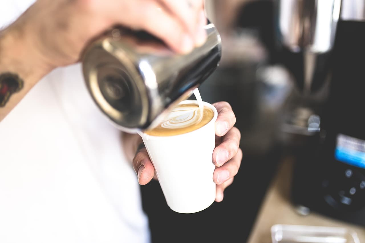 Barista pouring steamed milk into a takeaway cup